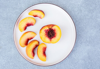 half ripe peaches and slices on a white plate on a gray background.