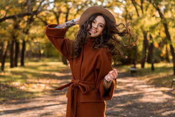 attractive stylish woman walking in park dressed in warm brown coat