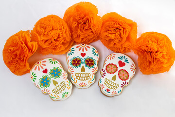 Cookies with shapes of Mexican catrinas and orange marigold flowers to celebrate Halloween or Day of the Dead on white background