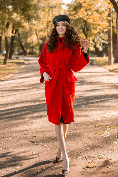 attractive stylish woman walking in park dressed in warm red coat