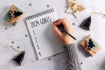 Female hands writing goals 2024 in a notebook. Festive decoration on table. Flat lay. New Year's plans - 648082321