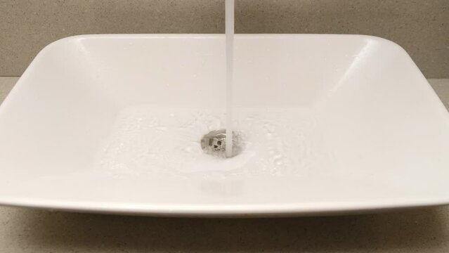 White bathroom sink on an black wooden countertop with a soap dispenser