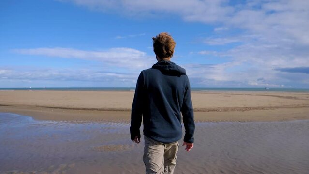 slow motion shot of a man walking across a beach at low tide near the Sete salt flats