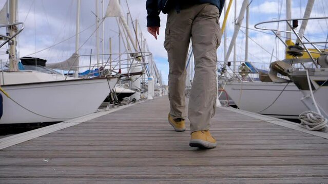 Slow motion low-angle shot of a man walking along a marina dock toward a yacht - Powered by Adobe