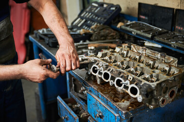 Close up of strong worker holding instrument, equipment by dirty hands. Hardworking male wearing uniform, working in garage, workshop, servicing center. Concept of manual labor.