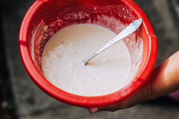 A woman, a cook, holds in her hands a red plastic bowl with batter, dough for baking. Food photography, top view.