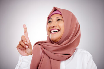 Pointing up, happy and face of Muslim woman in studio with makeup, cosmetics and beauty. Fashion, style and and Islamic person with hand gesture for news, promotion and show on gray background