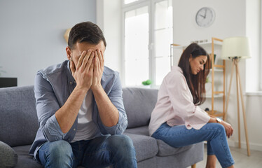 Upset married couple sitting silently on sofa facing away from each other. Stressed husband and...