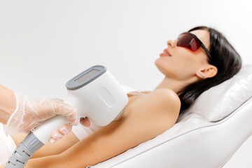 Body care concept. Laser hair removal. Young Caucasian woman in safety glasses lies on the sofa, female cosmetologist doing laser hair removal in a beauty salon