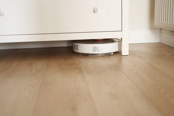 Wireless autonomous robotic vacuum cleaner vacuums with brushes under commode at living room....