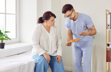 Male doctor orthopedist consulting overweight woman in medical office. Podiatrist showing insoles...