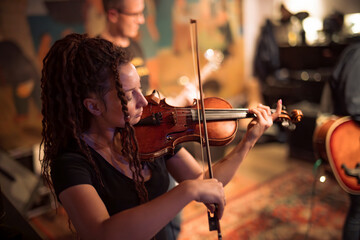 A female violinist plays the violin. Band performs on stage, rock music concert.