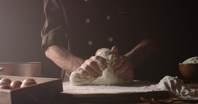 Closeup shot of hands of senior bakery chef applying flour on dough, old man kneading dough, making bread using traditional recipe, isolated on black background 