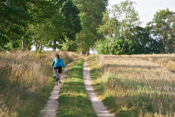 Fototapeta premium back view of a young woman riding a bicycle in the countryside. traveling by bike. outdoor activity.