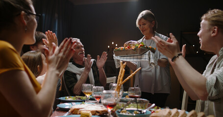 Large caucasian family celebrating thanksgiving day, chatting at dinner party table when senior woman brings roasted turkey to table. People applauding and happily smiling 4