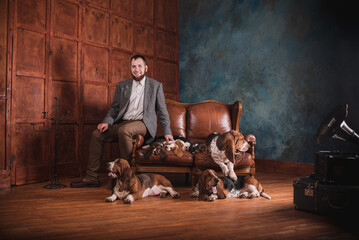 A man in an expensive suit with purebred basset dogs in an expensive stylish interior. A breeder with puppies and adult hunting dogs in his office with a leather sofa and wood paneling