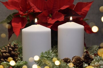 Two large white candles are burning against a background of red poinsettia and lights. 