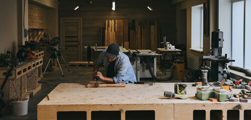 Carpenter works with wood in carpentry workshop. Man doing woodwork professionally
