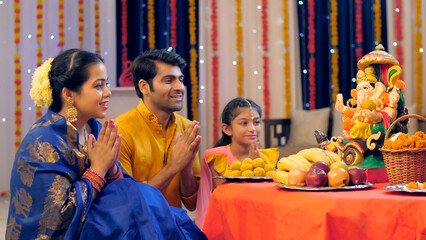 A nuclear Indian family in ethnic dress - praying on the occasion of Ganesh Chaturthi  Indian festival. Loving Indian family worshipping Lord Ganesha with puja ki thali - festival celebration  Indi... - obrazy, fototapety, plakaty