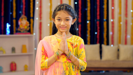 Diwali greetings by a young Indian girl  namaste greetings on the Diwali festival  Hindu religion  an auspicious occasion. An Indian child greeting in a Indian Namaste pose  colorful background  Di... - obrazy, fototapety, plakaty