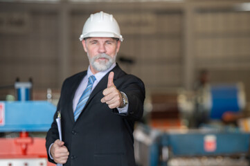older owner engineer with beard mustache on face standing smile with his arms crossed at construction factory site. Boss manager in suit show good thumb at factory industry site.