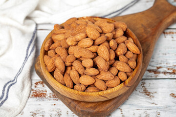 Almond in wood bowl. Roasted almonds on white wood background. Close up