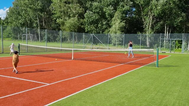 mother with kids playing tennis on court outdoors