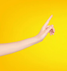 Female hand pointing at something isolated on yellow background with copy space.