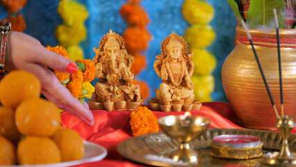 Lady offering marigold flowers to Lord Ganesha and Devi Laxshmi on Ganesh Chaturthi. Religious Pooja Thali - plate of sweets  and a Kalash. Hindu festival  Prayer in temple  Diwali Pooja