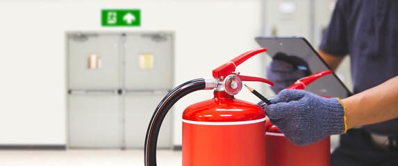Fire extinguisher has hand engineer checking pressure gauges with exit door to prepare fire equipment for protection in emergency case and safety or rescue and alarm system training concept.