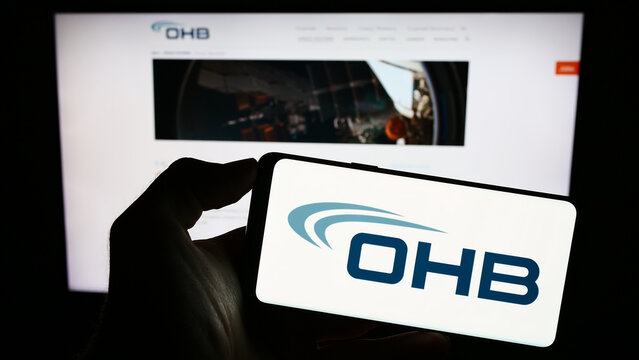 Stuttgart, Germany - 09-10-2023: Person holding cellphone with logo of German aerospace company OHB SE on screen in front of business webpage. Focus on phone display.