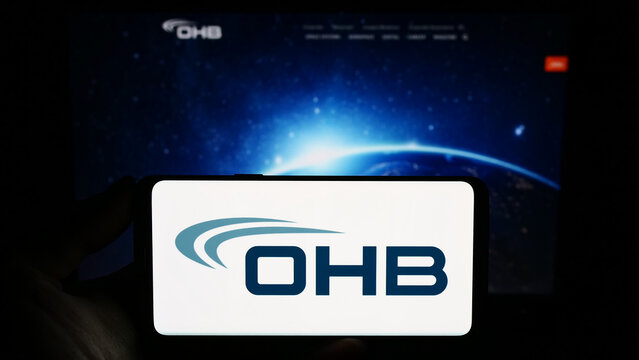 Stuttgart, Germany - 09-10-2023: Person holding smartphone with logo of German aerospace company OHB SE on screen in front of website. Focus on phone display.