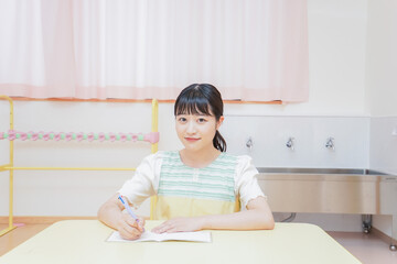 Naklejka premium 事務作業をする若い幼稚園教諭
