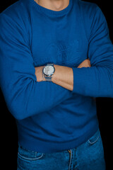 Man posing idly by with a wristwatch in a blue sweater, fashion and style of clothing on a dark background