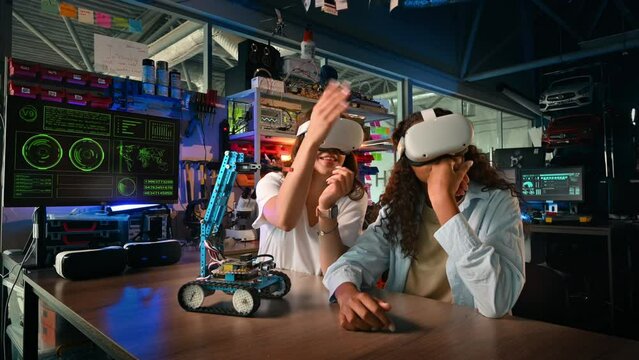 Two young women in VR glasses doing experiments in robotics in a laboratory. Talking. Robot on the table