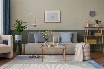 Zelfklevend Fotobehang Creative composition of cozy living room interior with mock up poster frame, modular sofa, blue pillows, wooden coffee table, patterned rug, beige wall and personal accessories. Home decor. Template. © FollowTheFlow