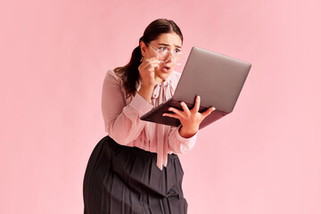 Emotive woman, employee attentively looking on laptop with shocked and worried face against pink...