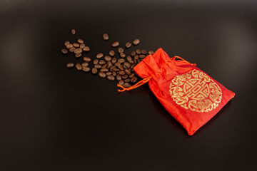 Coffee beans spilled from a red silk bag close-up with black background