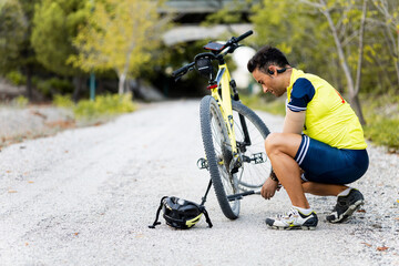 An adult male with an arm prosthesis is crouching using an air pump to inflate a mountain bike...