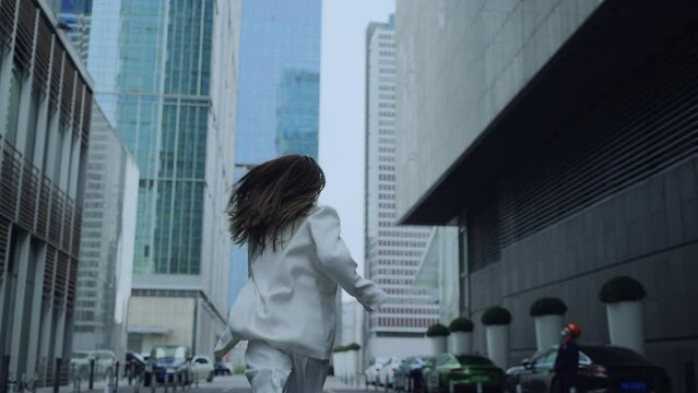 slow motion back view of young business woman in white suit running in the Urban Street under the high office building