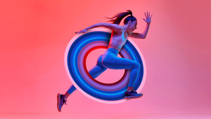 Young girl, athlete, runner in motion, training over pink studio background in neon light with...
