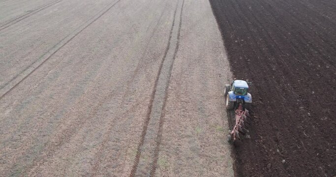 Farm tractor with cultivator works at agriculture field, aerial drone video