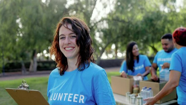 Young Latin volunteer working with group of people for food collection community service at City Park - Donations and charity Team project concept