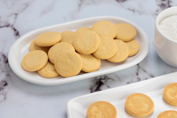 ingredients and mise en place for the preparation of cornstarch alfajores, filling the dulce de leche filling on top and grated coconut on the outside on white plates.