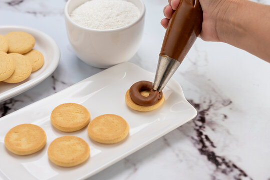 ingredients and mise en place for the preparation of cornstarch alfajores, filling the dulce de leche filling on top and grated coconut on the outside on white plates.