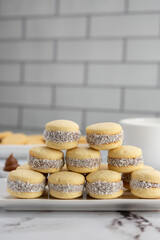 Homemade cornstarch alfajores filled with dulce de leche with coconut and cup of tea on plates and white background