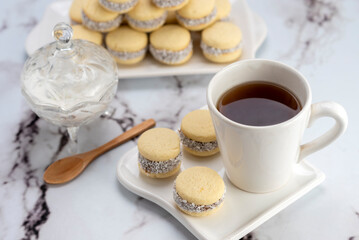 Homemade cornstarch alfajores filled with dulce de leche with coconut and cup of tea on plates and white background