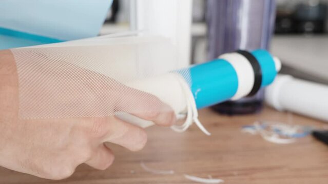 A man is holding a cut open reverse osmosis water membrane filter on a table and is unwinding its layers to inspect them.