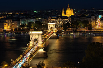 Night light landscape of Budapest. Illuminated Chain Bridge over Danube river and embankment with vintage buildings in the background. Famous touristic place and romantic travel destination