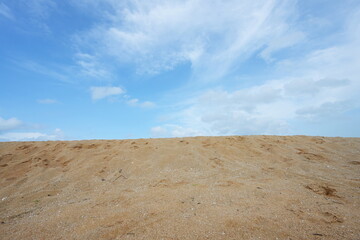 Image of sand dunes, sky and scattered white clouds during day in a summer. The sand has footprints of people passing through the area. Divide the area of ​​the sand dune and sky equally in half.
